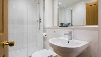 Een moderne badkamer met een douchecabine van glas, een witte wastafel en een toilet.