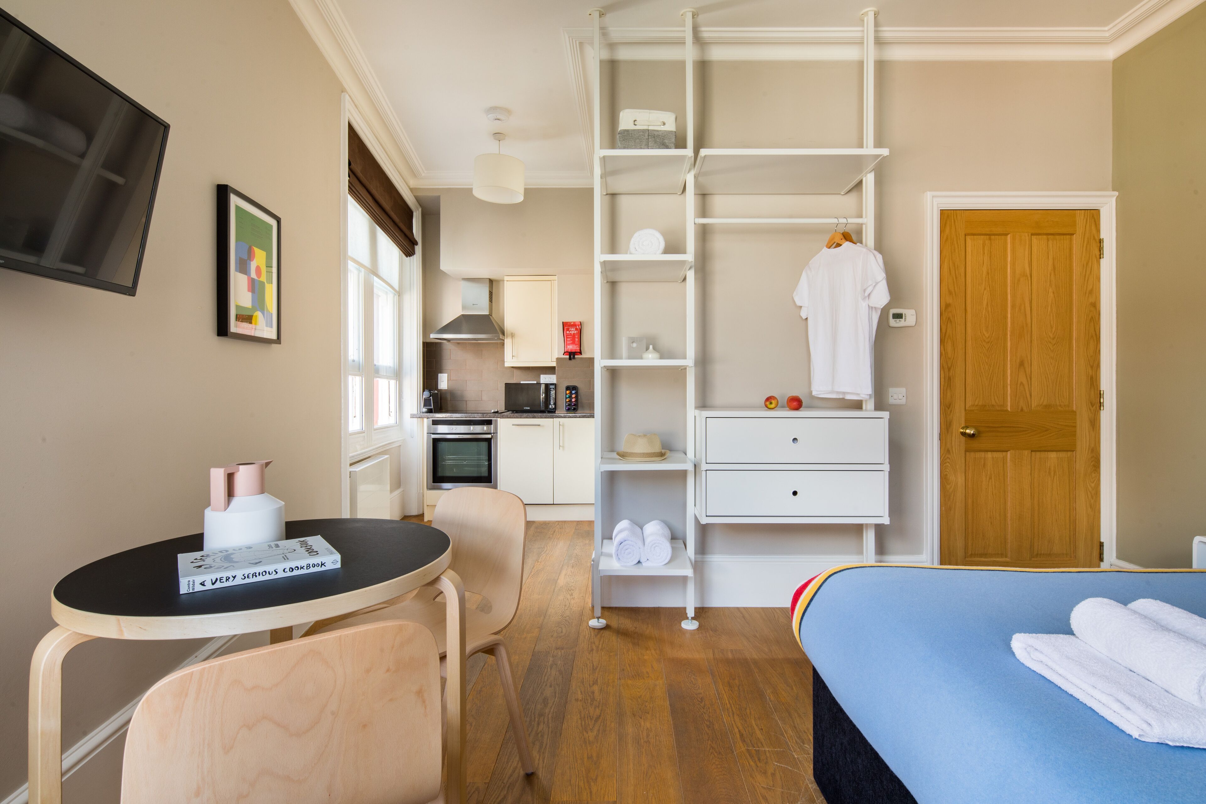 Ein kleines Hotelzimmer mit Bett, Schreibtisch, Stuhl, einer Küchenzeile und einem Kleiderschrank.