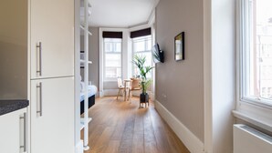 A narrow hallway with a kitchen area on the left, a dining area with a table and chairs in the center, and a large window on the right. - Hausd - Covent Garden (London)