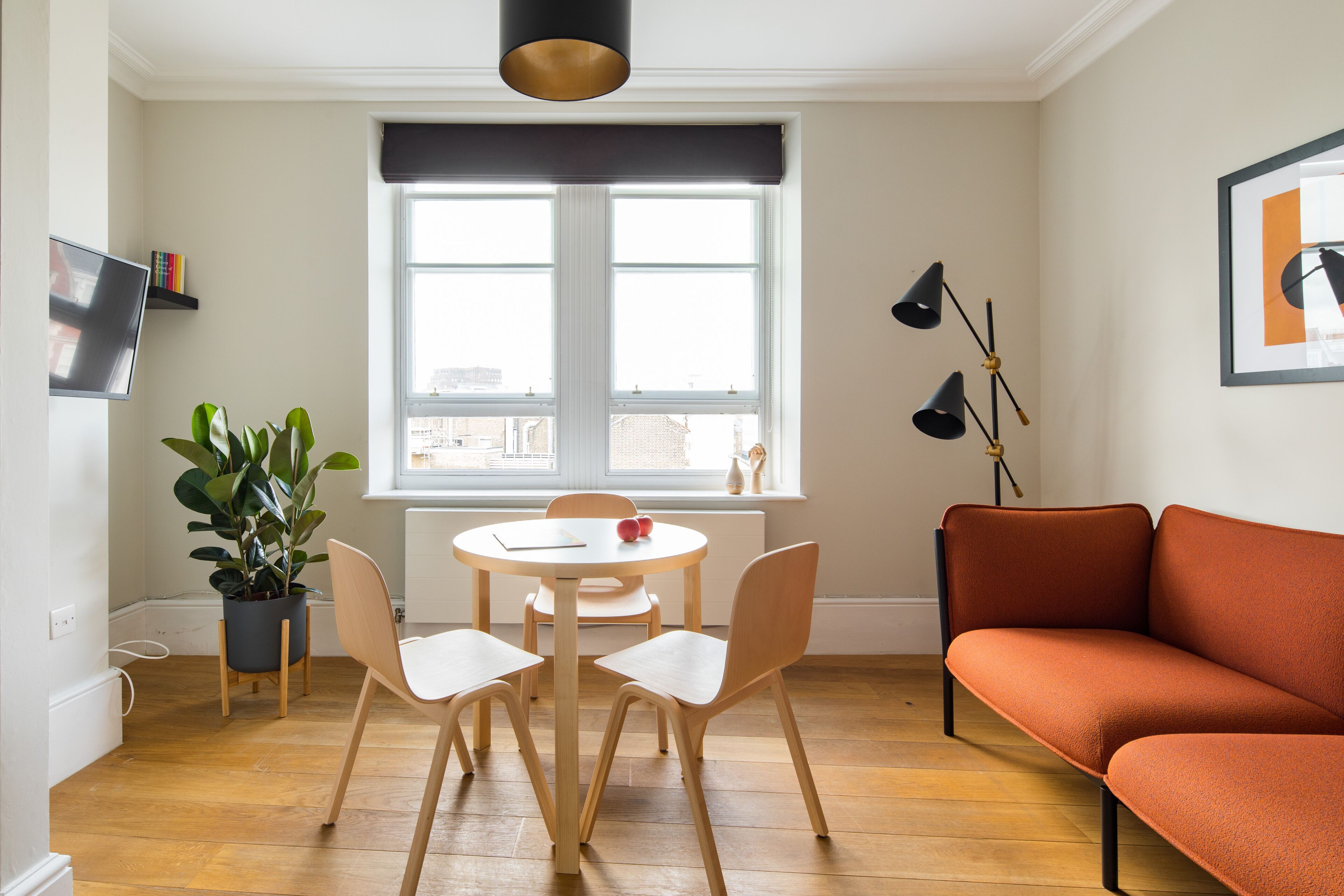 A modern living room with a round table, two chairs, a sofa, a potted plant, and a large window with a view of the city.