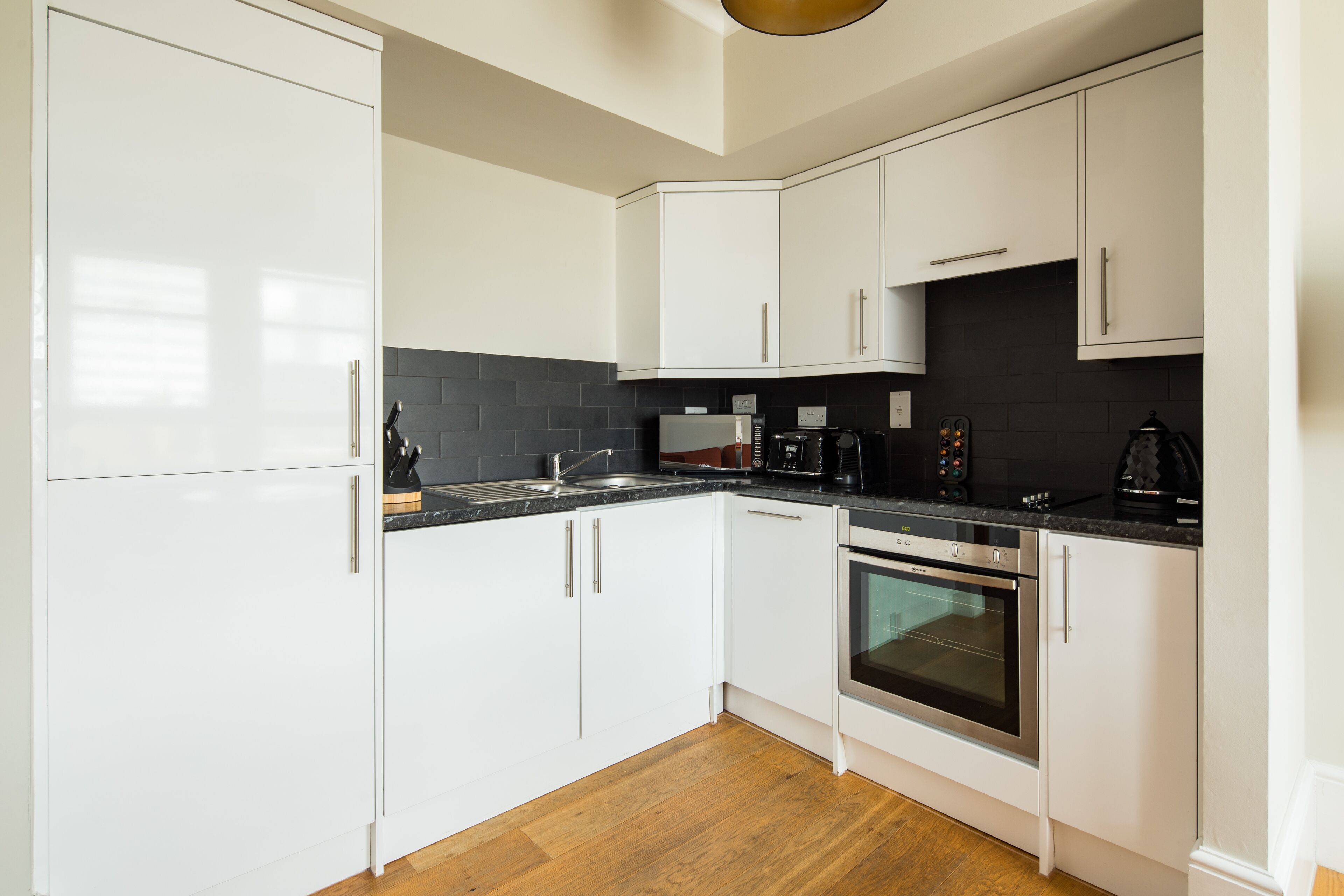 A modern kitchen with white cabinets, a black countertop, and a wooden floor.