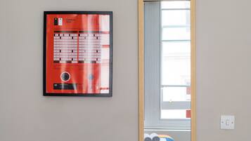 A framed chart on the wall, a window with blinds, and a bed with rolled towels.