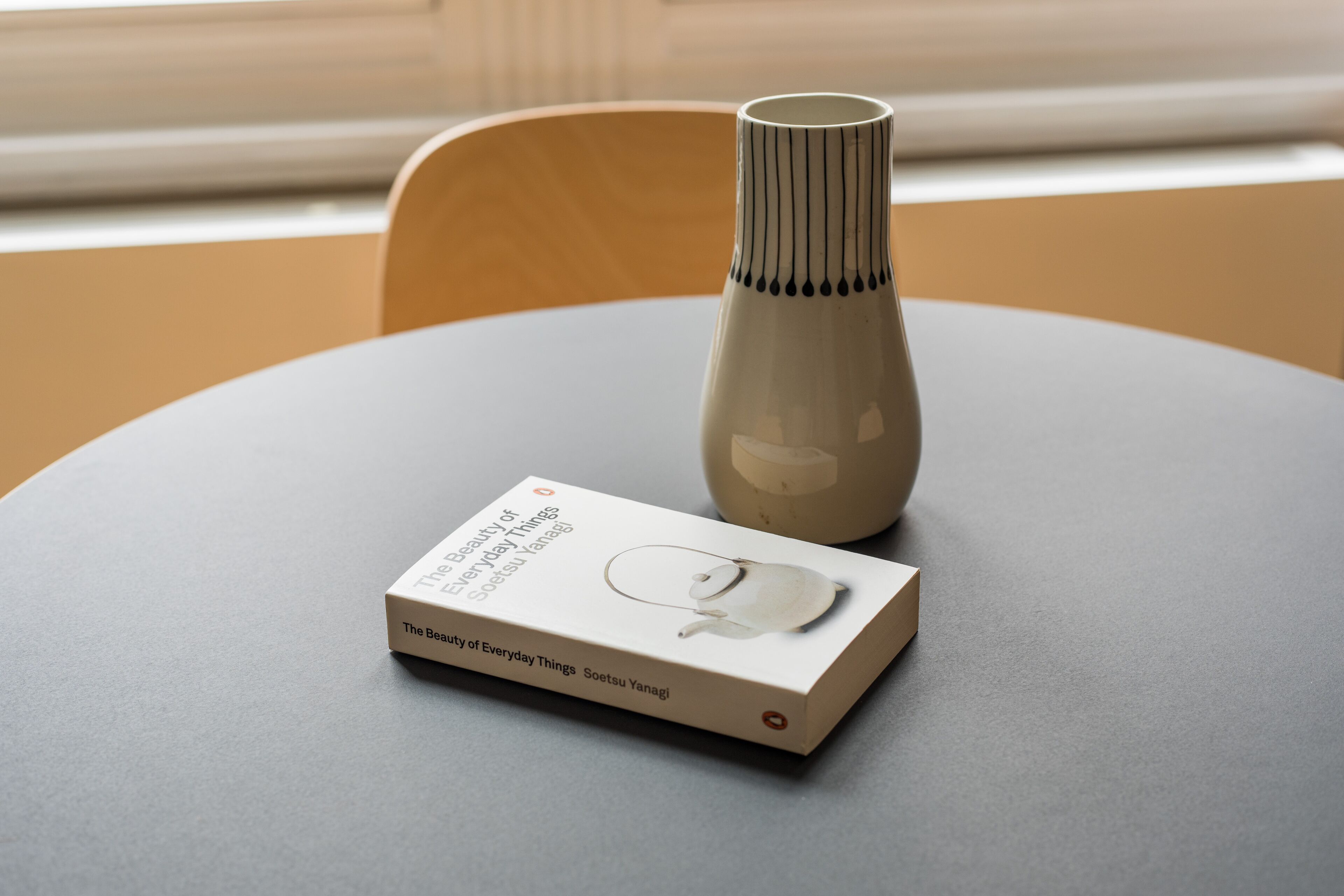 A book titled "The Beauty of Everyday Things" by Soetsu Yanagi on a table with a vase.