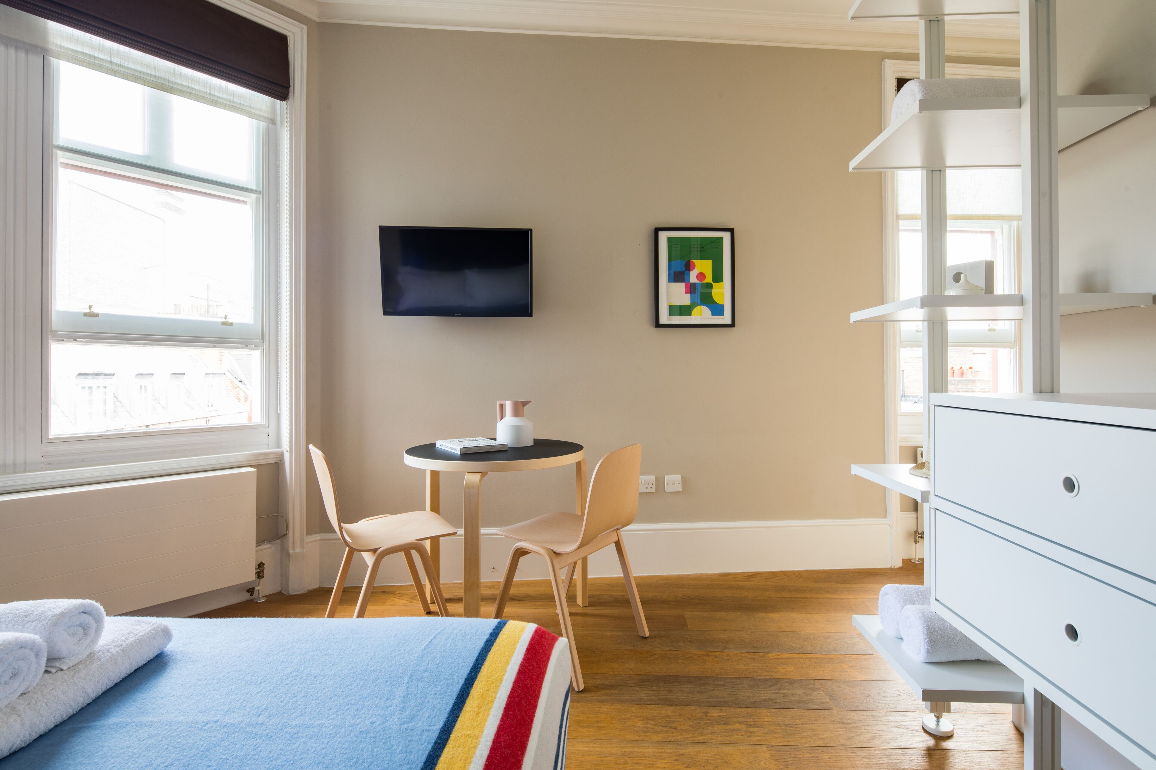 Ein Hotelzimmer mit Bett, Schreibtisch, Stuhl, Fernseher und einem gerahmten Bild an der Wand.
