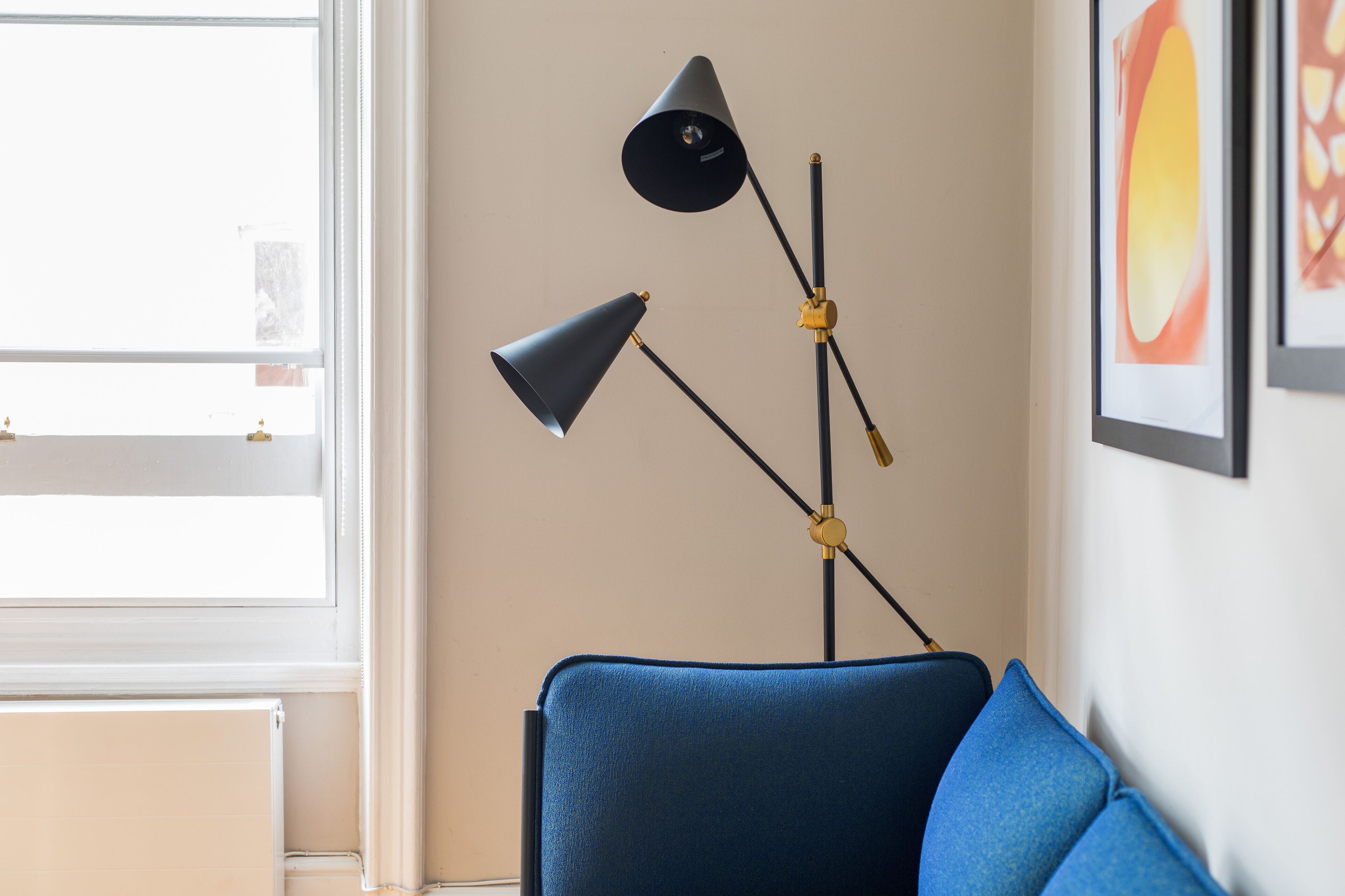 A room with a blue armchair, a floor lamp, and a framed picture on the wall.