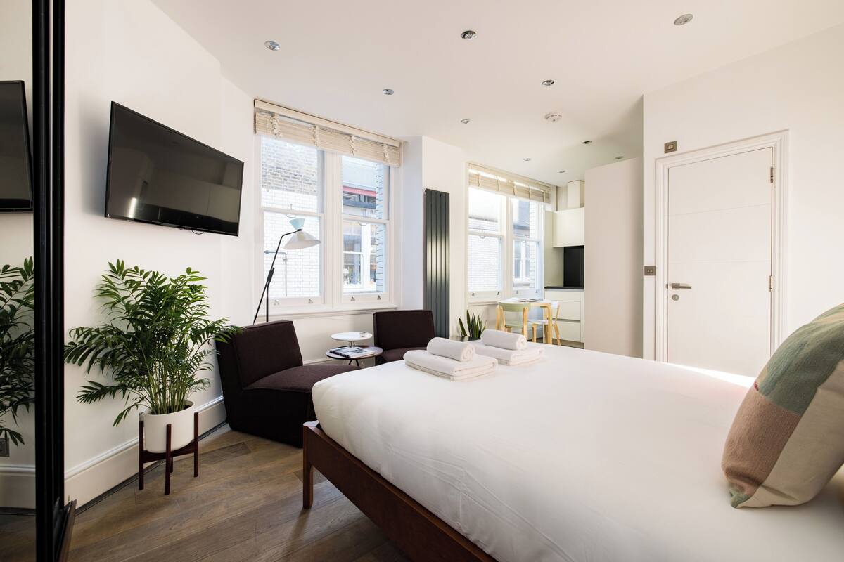 Ett modernt hotellrum med en stor säng, en platt-TV, ett skrivbord och en sittgrupp med en stol och ett litet bord.