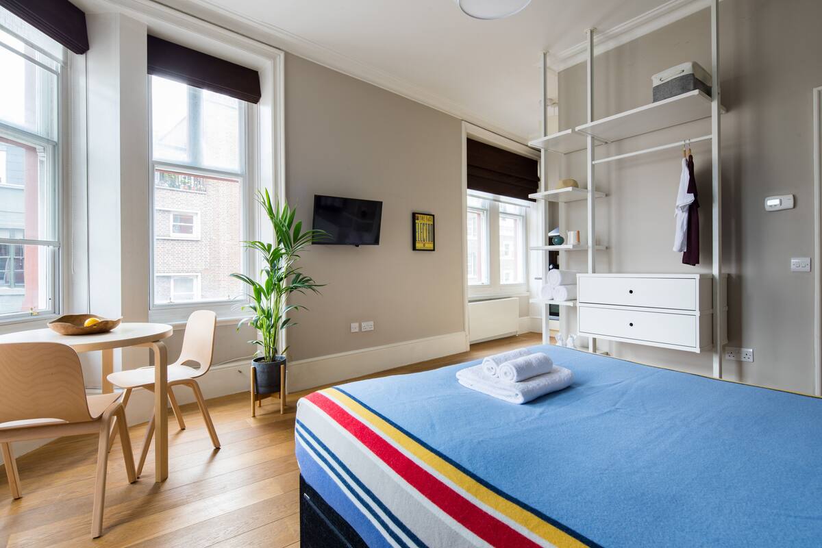 Ett hotellrum med en säng, ett skrivbord, en stol, en krukväxt och en tv på väggen.