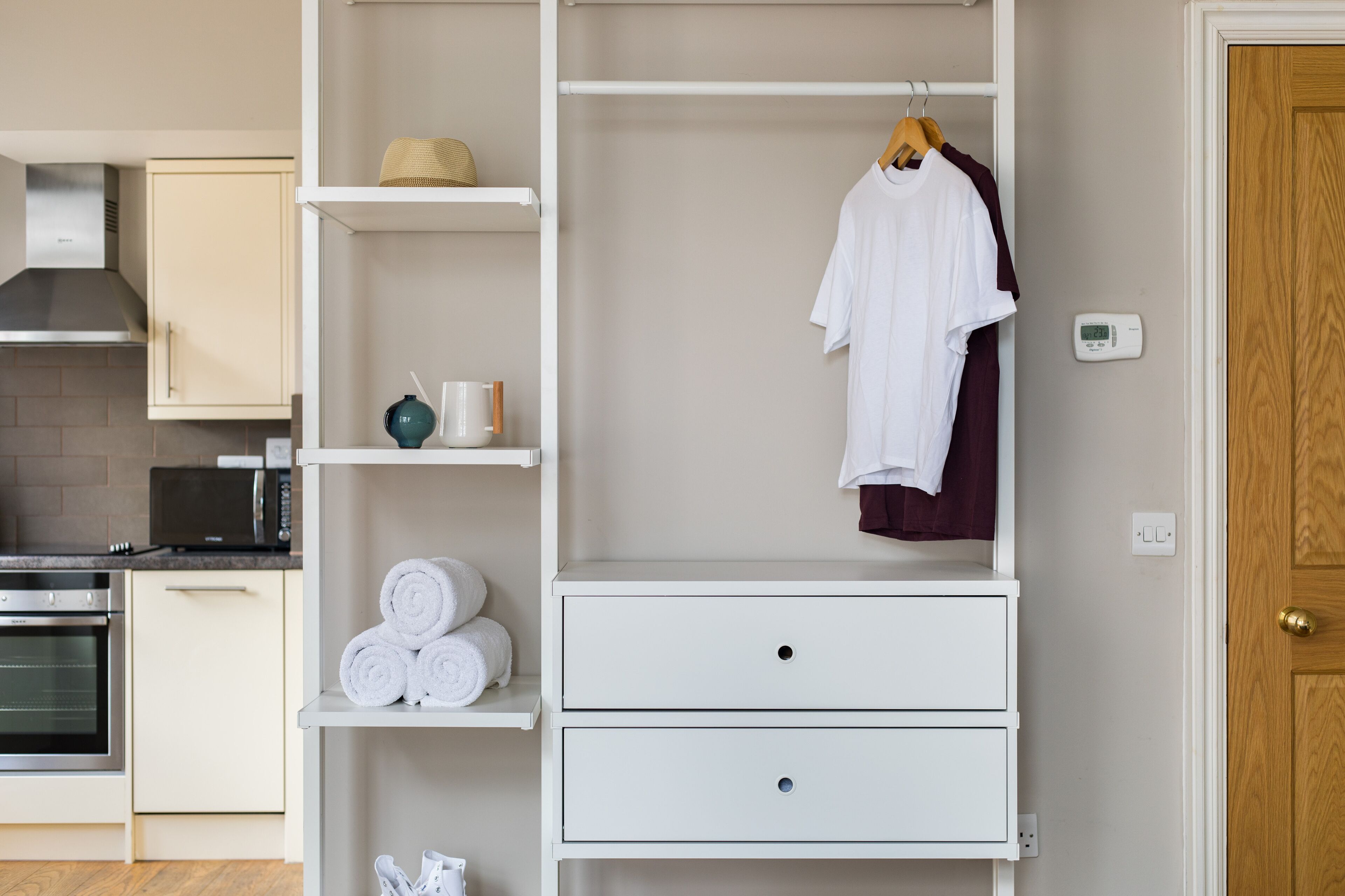 A modern kitchen with white cabinetry, a microwave, and a stove. There are towels and a hat on a shelf.