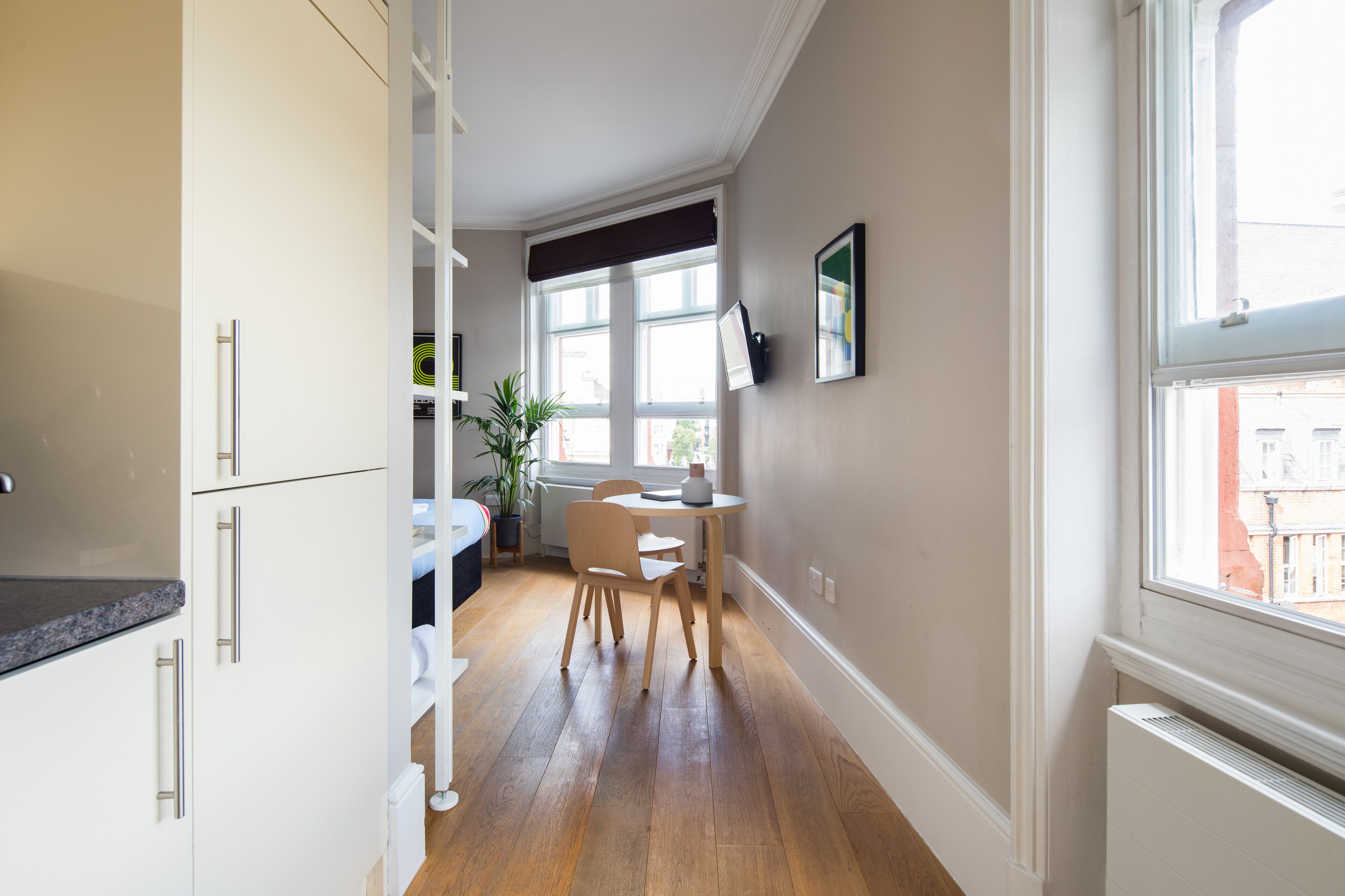 Una cocina estrecha con armarios blancos, una mesa de comedor de madera y una ventana con vista a edificios.