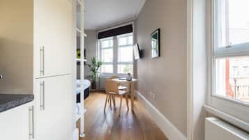Una cocina estrecha con armarios blancos, una mesa de comedor de madera y una ventana con vista a edificios.