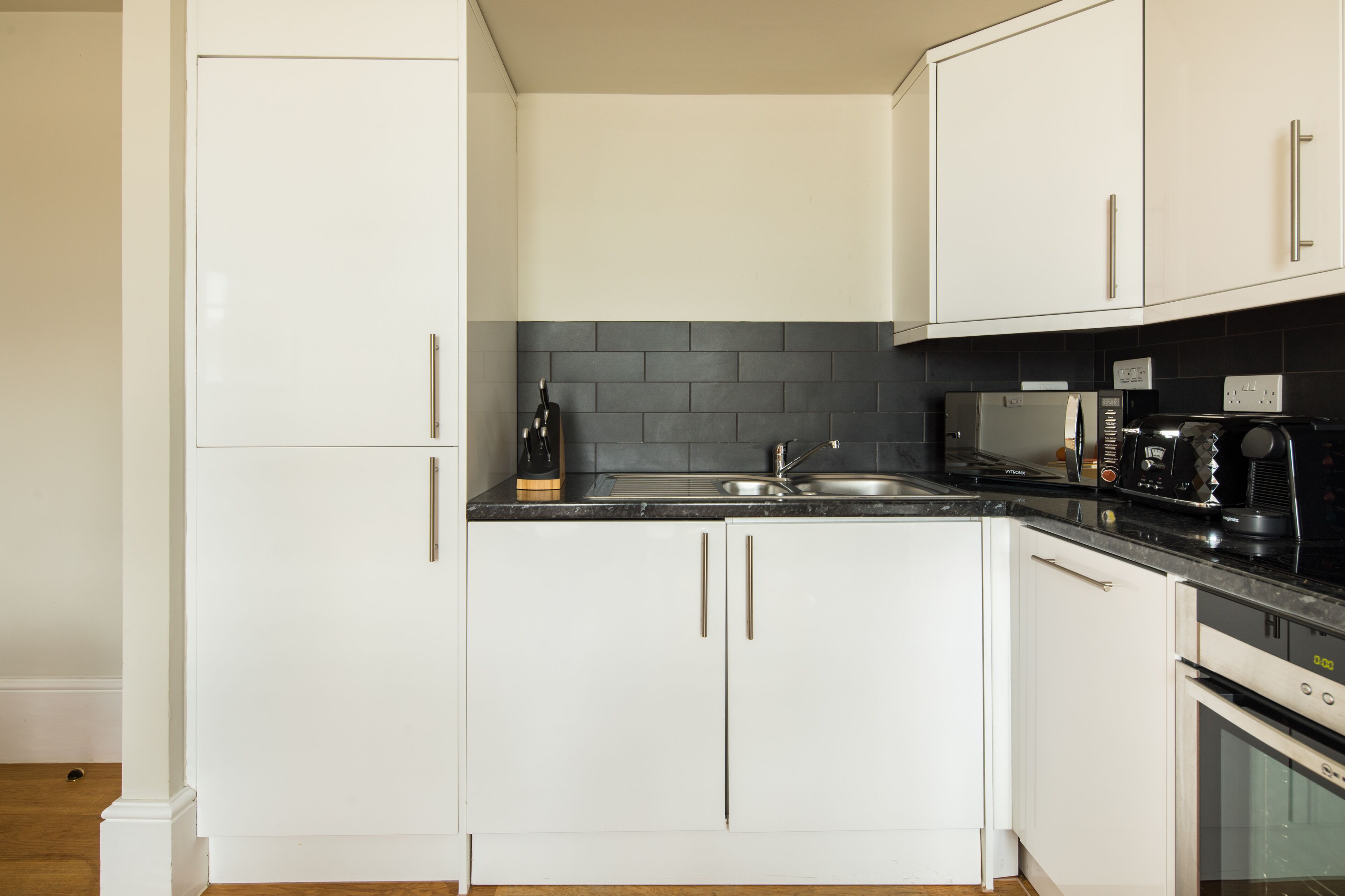 A modern kitchen with white cabinets, a black countertop, a built-in microwave, and a stove.