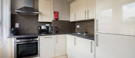 A modern kitchen with white cabinets, a stainless steel range hood, a built-in oven, a coffee maker, and a sink.