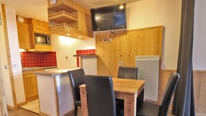 Une cuisine de taille réduite avec des meubles en bois, un four à micro-ondes, un pare-feu en carreaux rouges, une table à manger en bois avec quatre chaises et un téléviseur encastré.