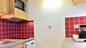 Une cuisine compacte avec des meubles en bois, un four à micro-ondes, un lave-vaisselle et des murs recouverts de carreaux rouges.
