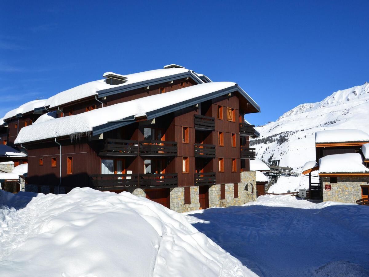 Un immeuble en bois à plusieurs étages, doté de balcons, entouré de montagnes enneigées.