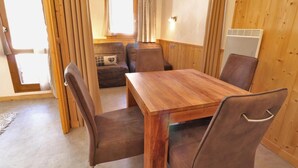 A cozy room with a wooden table and four chairs, a window with curtains, and a sliding door. - 10m from ski slopes, Ground floor, view limited, 27m², Méribel-Mottaret (Méribel - Les Allues)