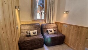 Two leather armchairs with heart-patterned cushions in a room with wooden paneling and a window with curtains. - 10m from ski slopes, Ground floor, view limited, 27m², Méribel-Mottaret (Méribel - Les Allues)