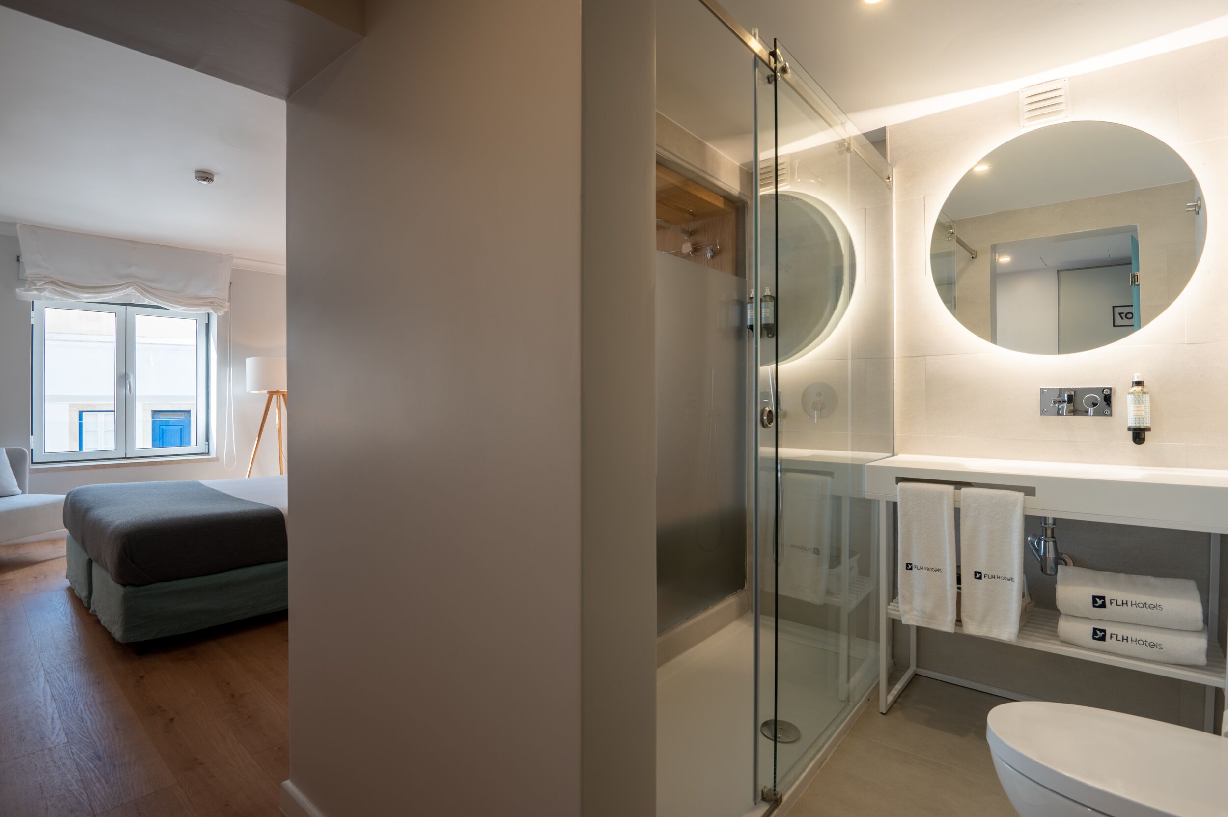A modern bathroom with a glass-enclosed shower, a round mirror, and a white sink with towels.