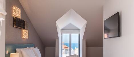 Un dormitorio con cama, mesita de noche, televisor y vistas al mar a través de una ventana.