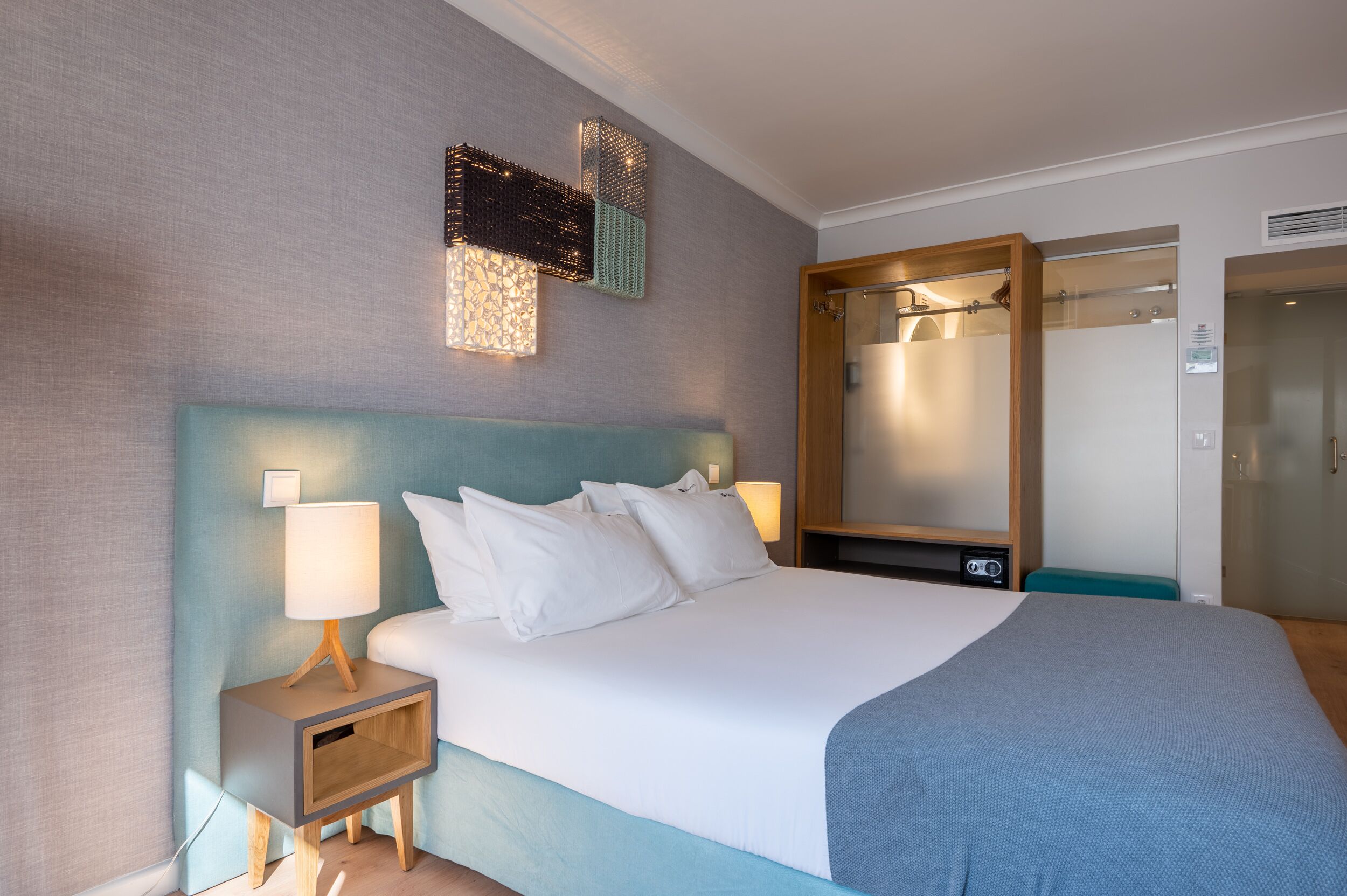 Et hotelværelse med en stor seng, et natbord med lampe, et spejl og et klædeskab.