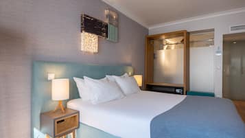 Et hotelværelse med en stor seng, et natbord med lampe, et spejl og et klædeskab.