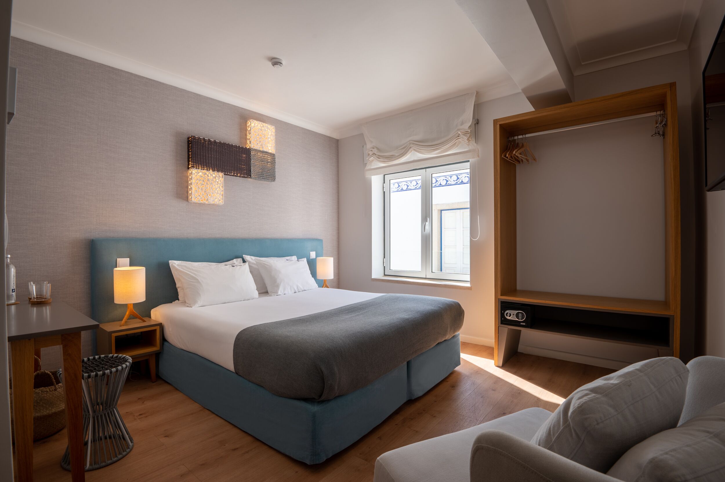 Une chambre d’hôtel avec un grand lit, une table de chevet avec une lampe, une chaise, un meuble pour la télévision et une fenêtre avec des rideaux.