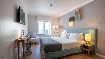 A hotel room with a bed, bedside table, lamp, and a window with curtains.