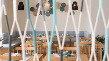 A restaurant interior with wooden tables and chairs, hanging pendant lights, and a wall decorated with circular wooden pieces.