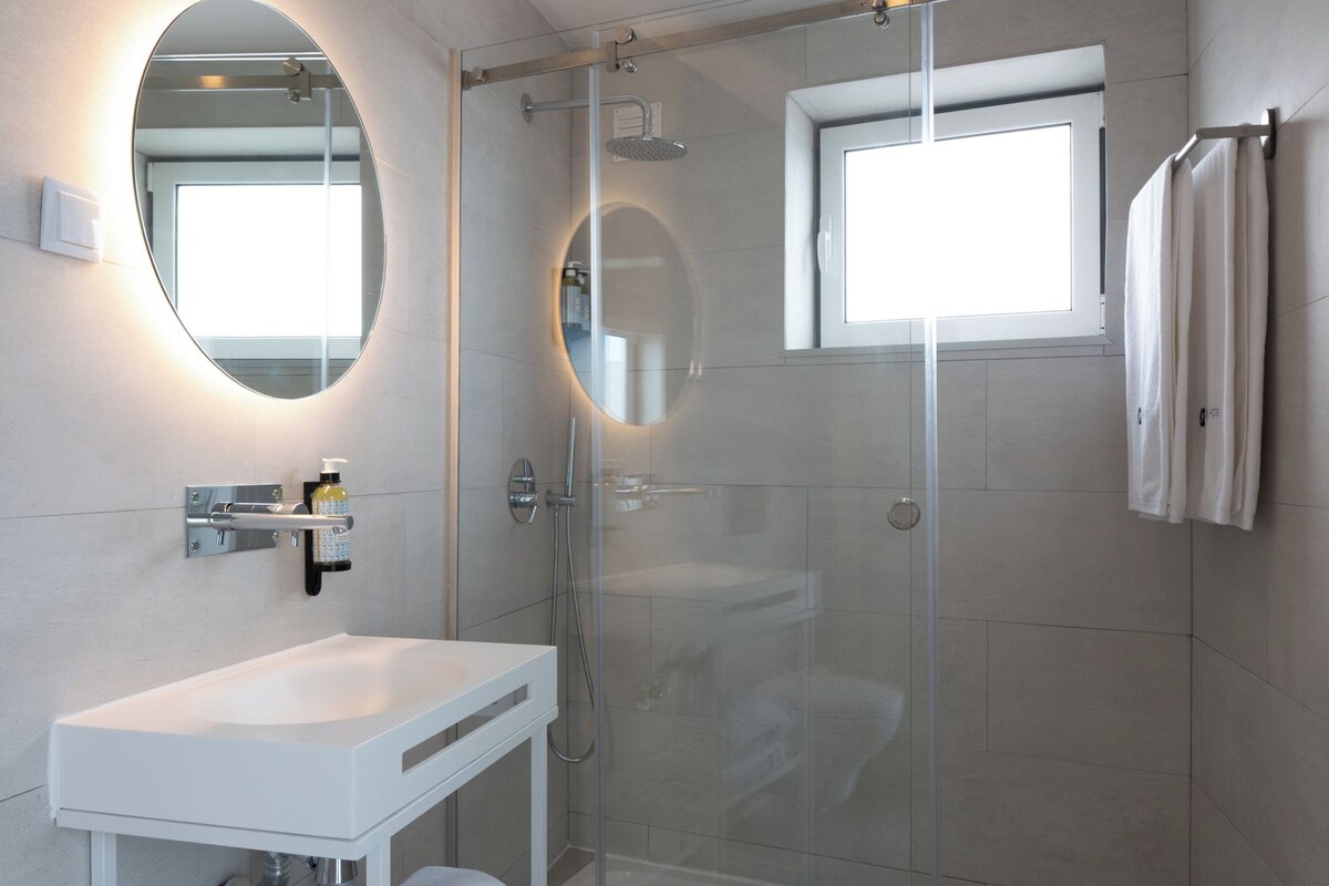 Un baño moderno con ducha de vidrio, lavamanos blanco y espejo.