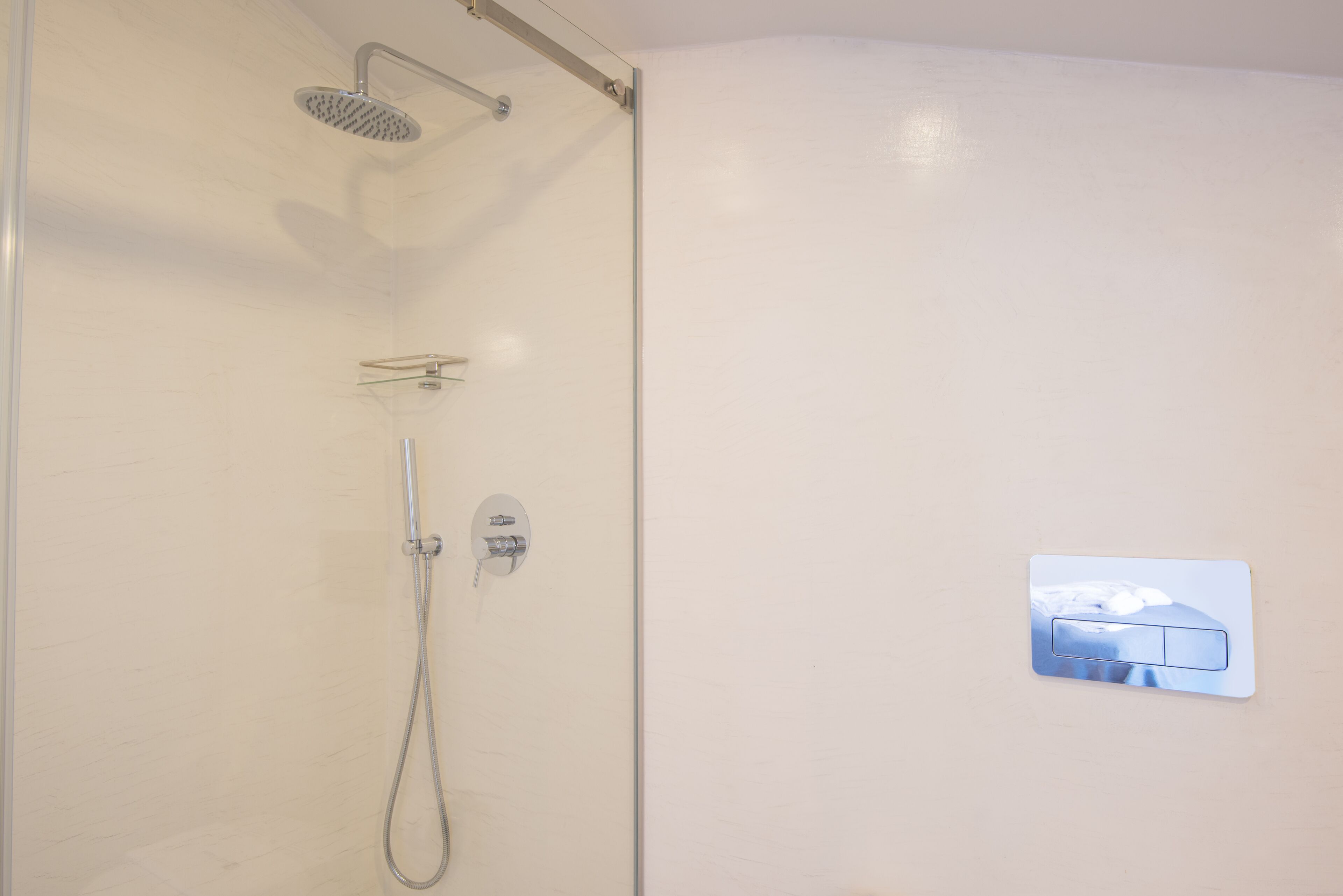 A shower with a handheld showerhead and a wall-mounted control panel.