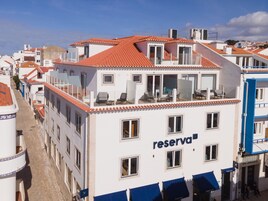 Un hotel con techo de tejas rojas, balcones con mobiliario exterior y un letrero que dice "reserva".