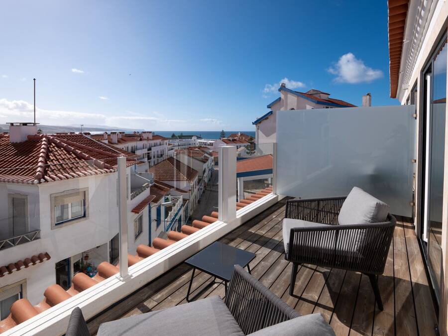 A balcony with a view of the sea, a table, and two chairs.