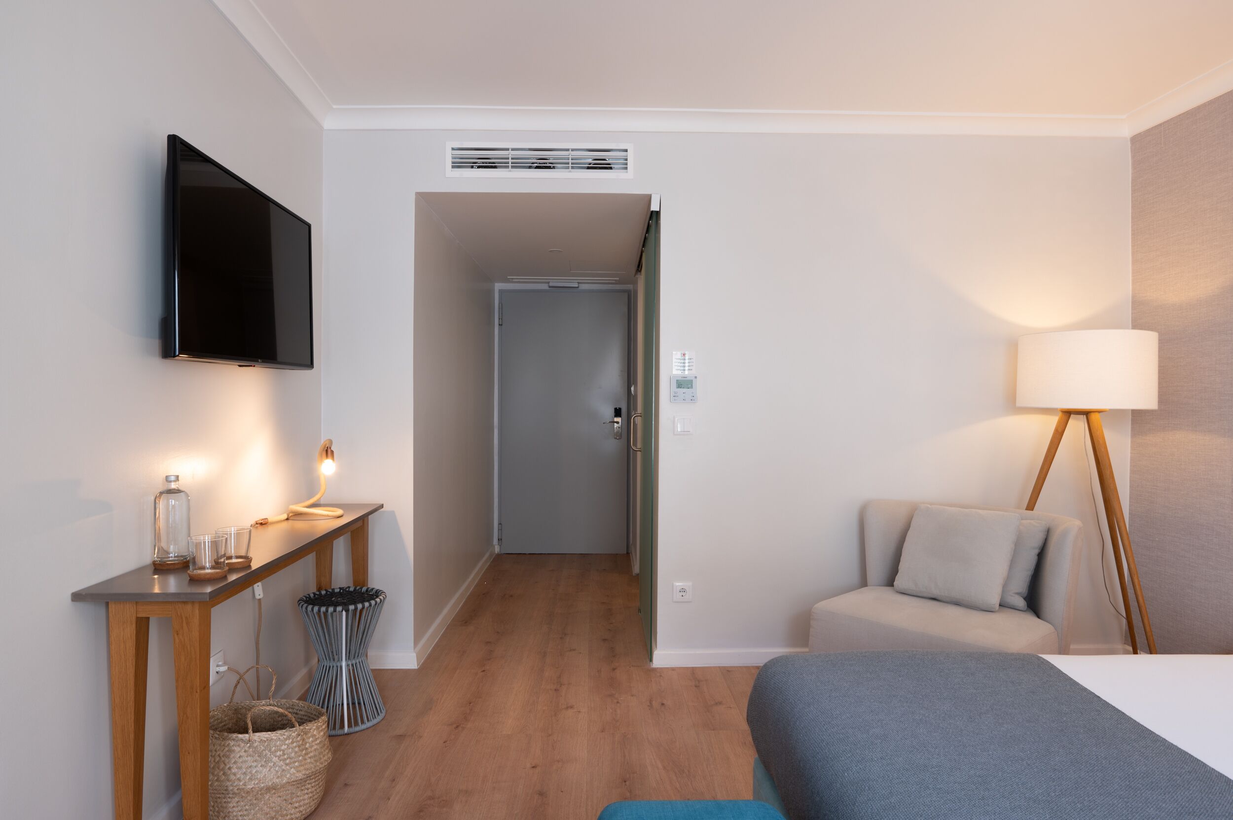 Una habitación de hotel moderna con un televisor de pantalla plana, una mesita de noche con lámpara, un sofá y una cama.