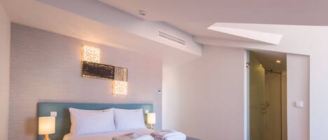 Una habitación de hotel moderna con una cama grande, una mesita de noche, una lámpara de pared y una puerta de ducha de vidrio.
