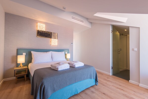 Una habitación de hotel moderna con una cama grande, una mesita de noche, una lámpara de pared y una puerta de ducha de vidrio.