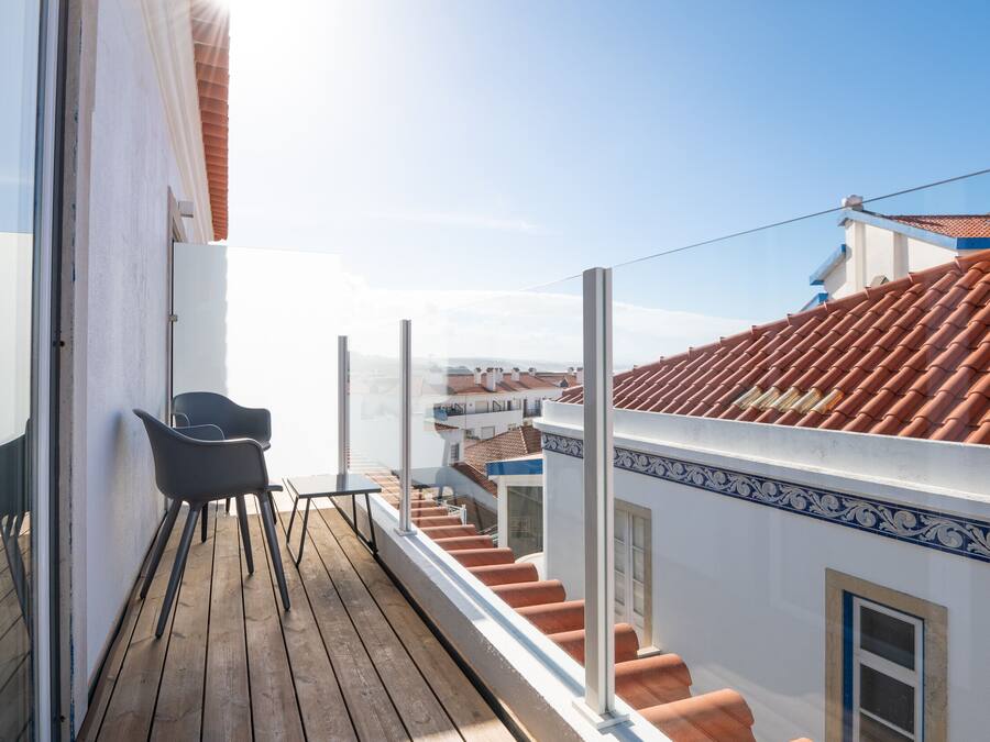 A balcony with a wooden floor, a chair, and a view of terracotta-roofed buildings.