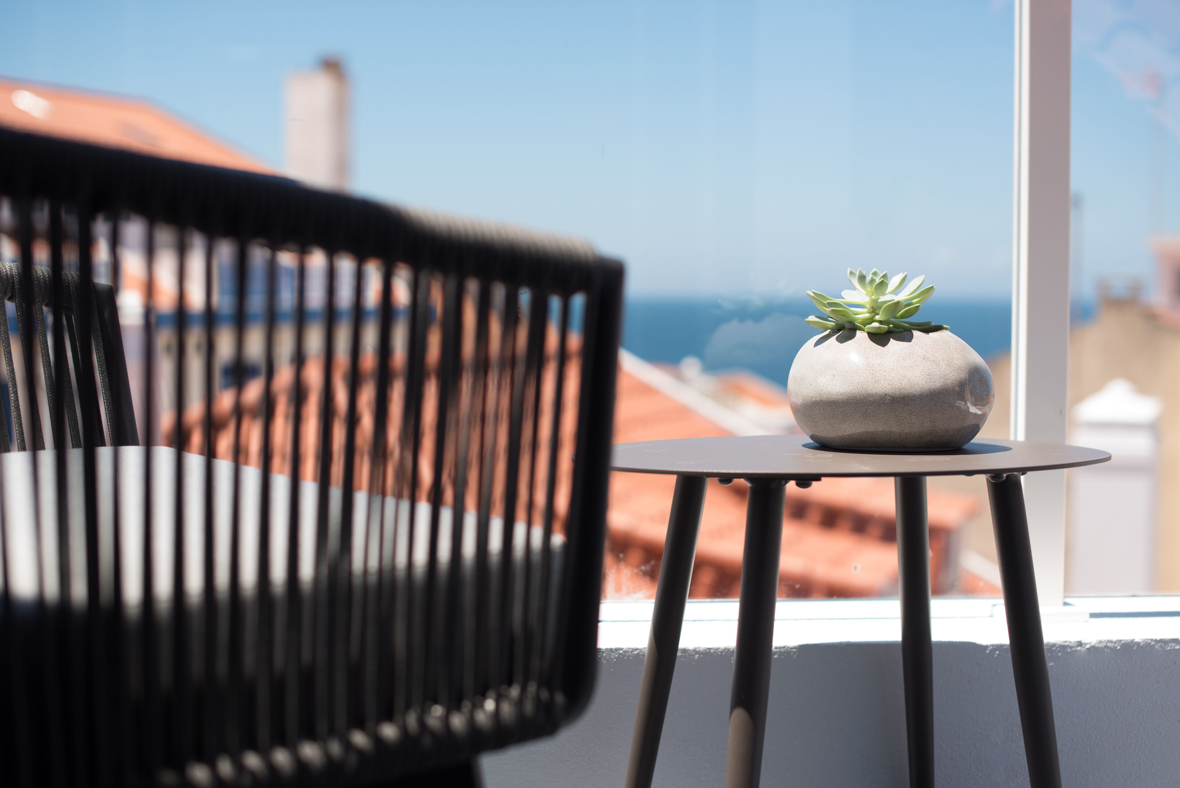 A modern chair and a small table with a potted plant on a balcony overlooking a cityscape.