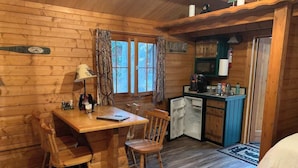 A cozy cabin interior with a wooden dining table, two chairs, a small kitchenette, and a bed.