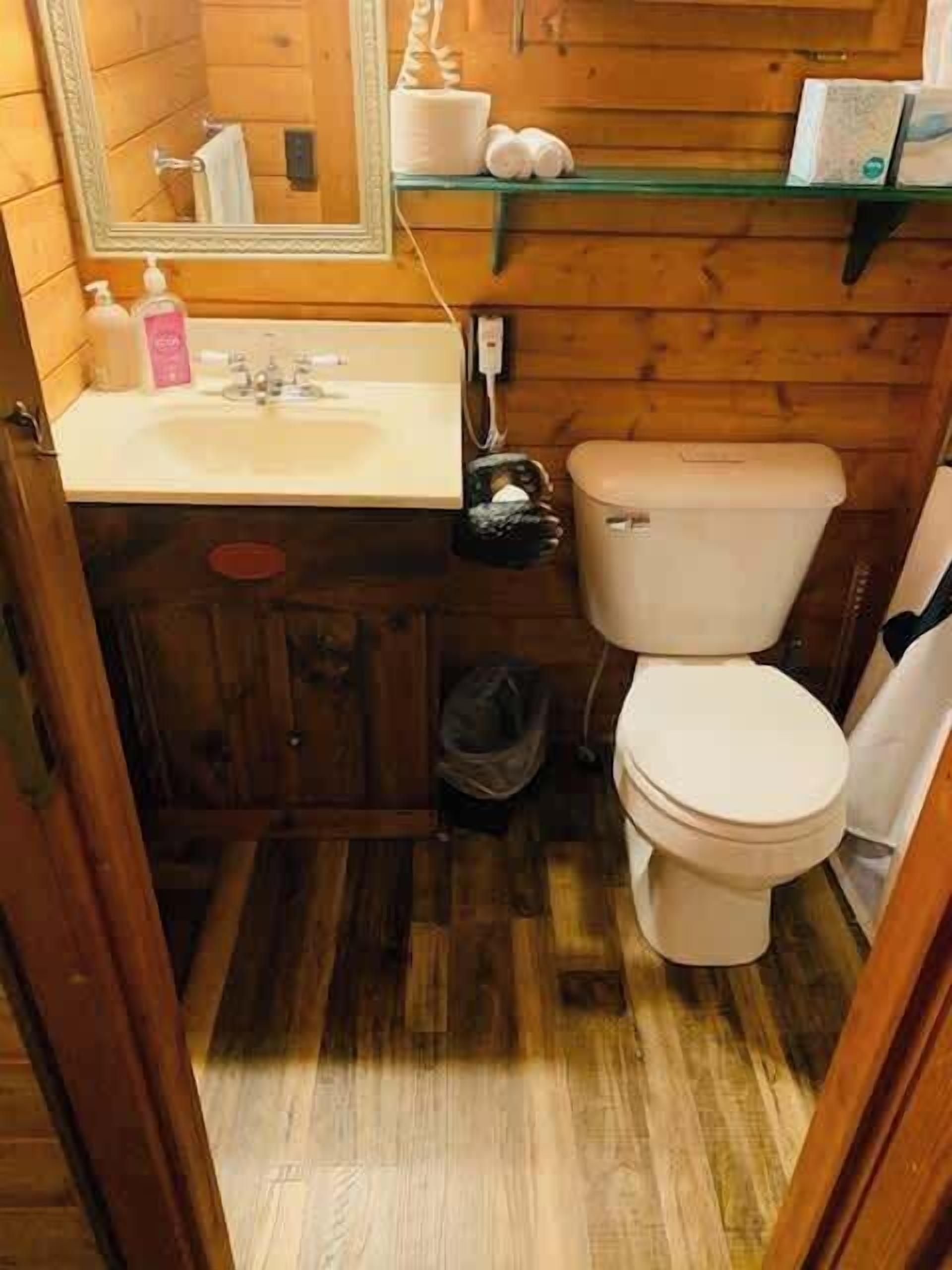 Un baño de madera pequeño y funcional con lavamanos, inodoro y espejo.