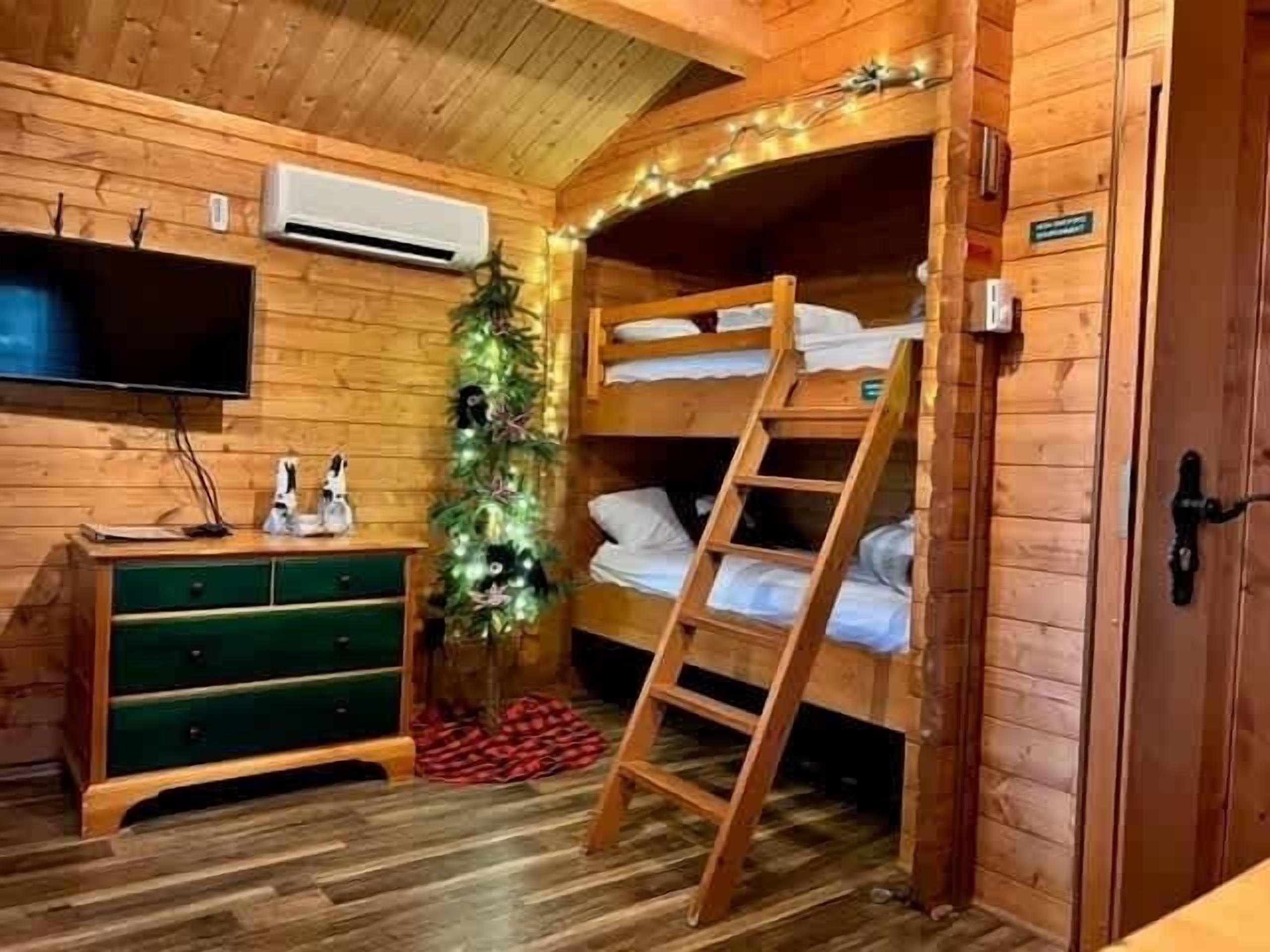 Une chambre dans un chalet en bois, avec des lits superposés, une télévision, une commode et un sapin de Noël.
