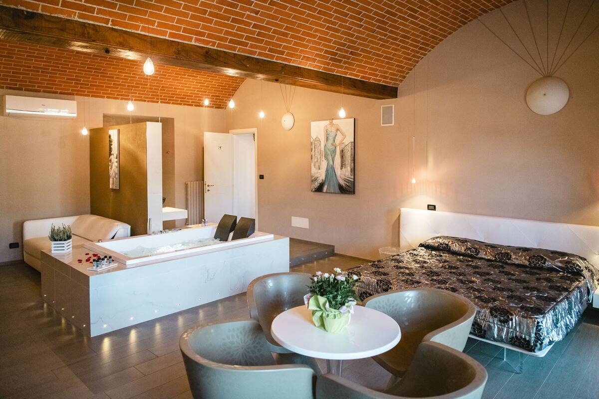 Una habitación de hotel moderna con una cama grande, un área de estar con una mesa y sillas, una bañera y un espejo amplio.