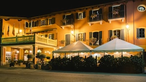 Een hotel met een balkon, een terras en een goed verlichte gevel.