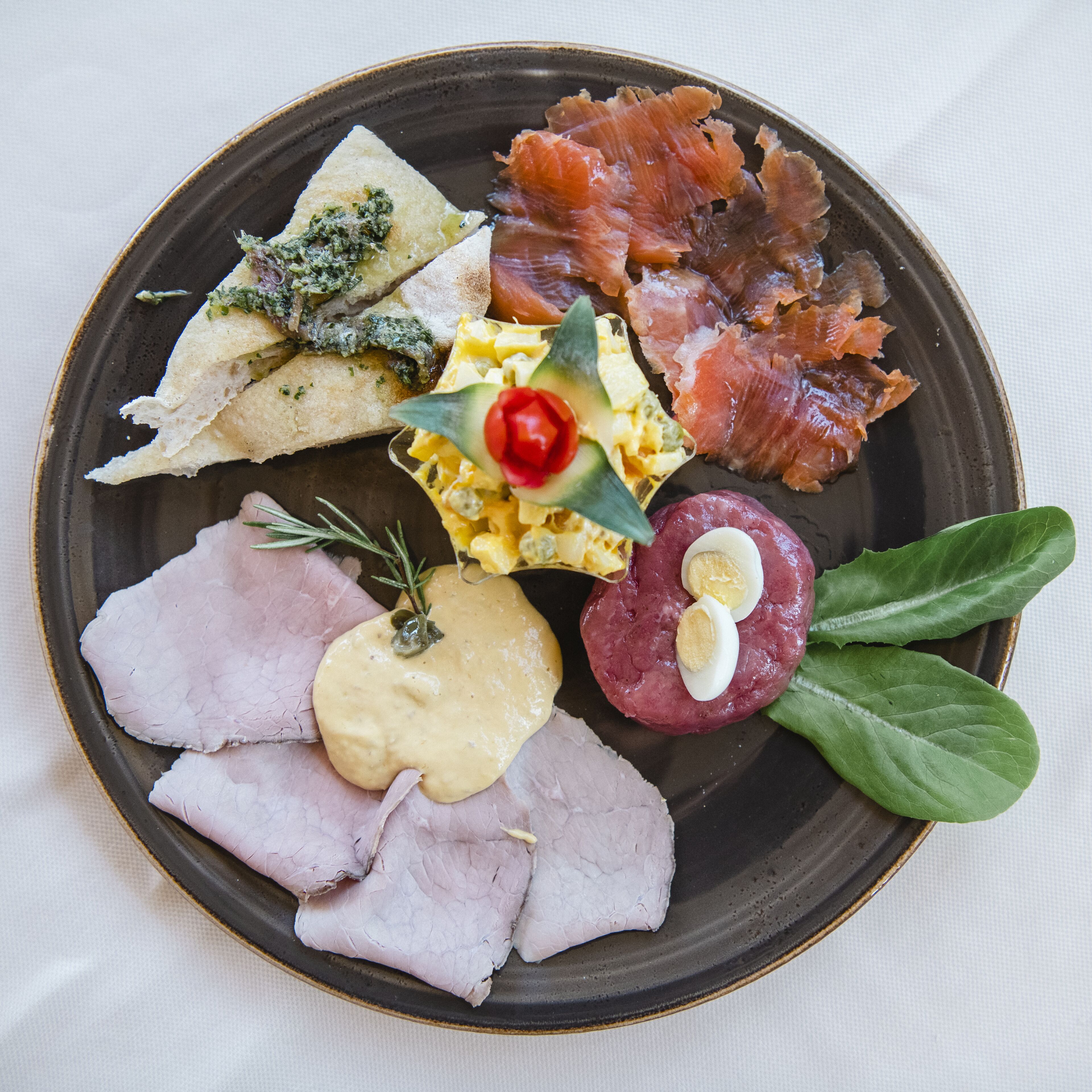 Ein Teller mit verschiedenen Speisen, darunter Räucherlachs, Käse und Fleisch.
