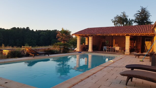 Piscina con sillas de descanso, un porche cubierto y vistas a árboles.