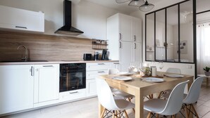 Une cuisine moderne avec des meubles blancs, un plan de travail en bois et un coin repas comprenant une table en bois et des chaises blanches.