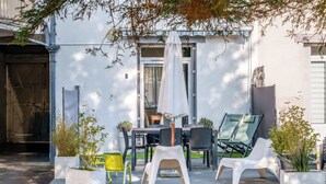 Une terrasse extérieure avec une table et des chaises, un parasol blanc et des plantes en pot.