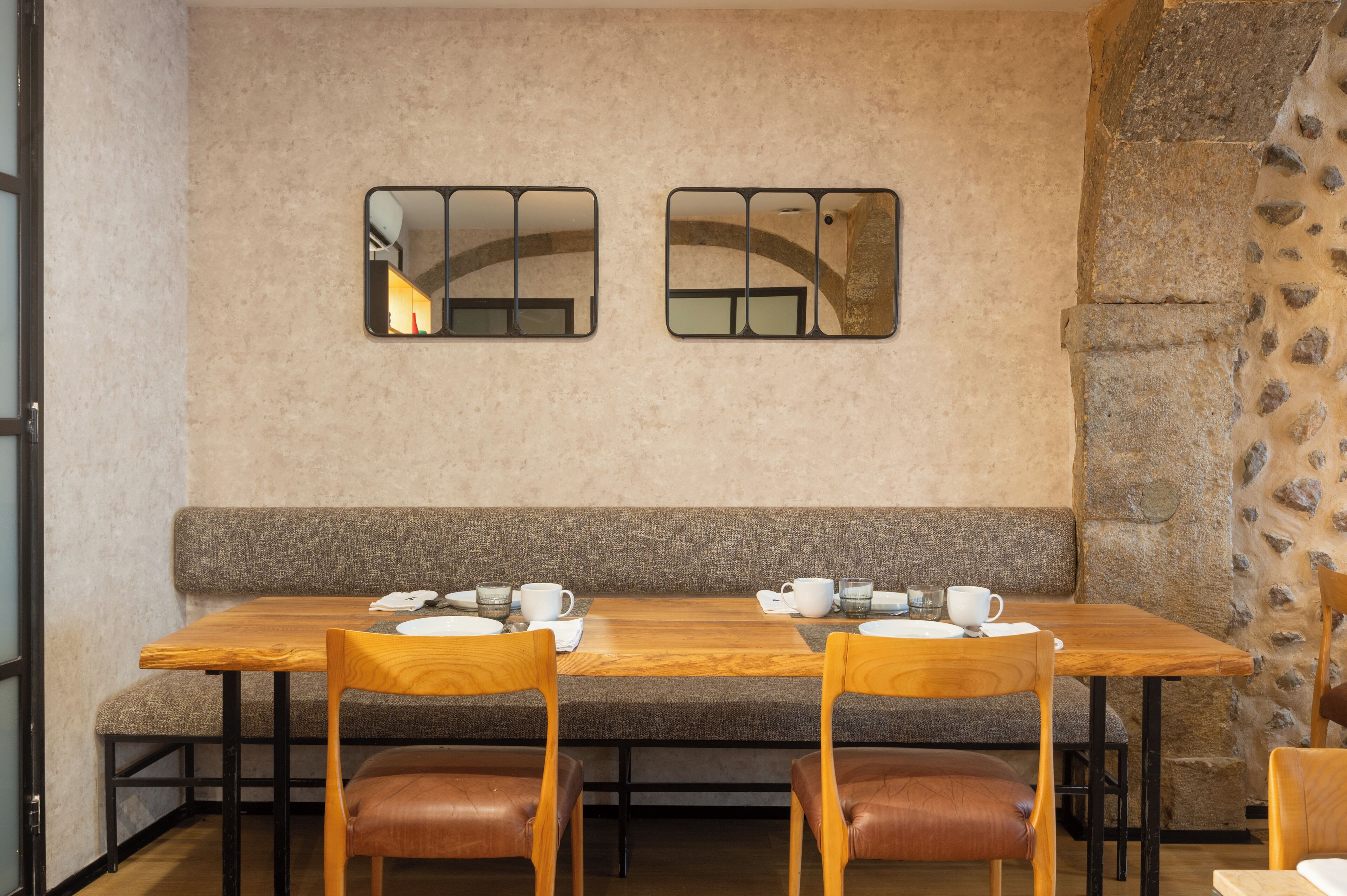 Un espace repas comprenant une table et des chaises en bois, un banc et deux miroirs fixés au mur.