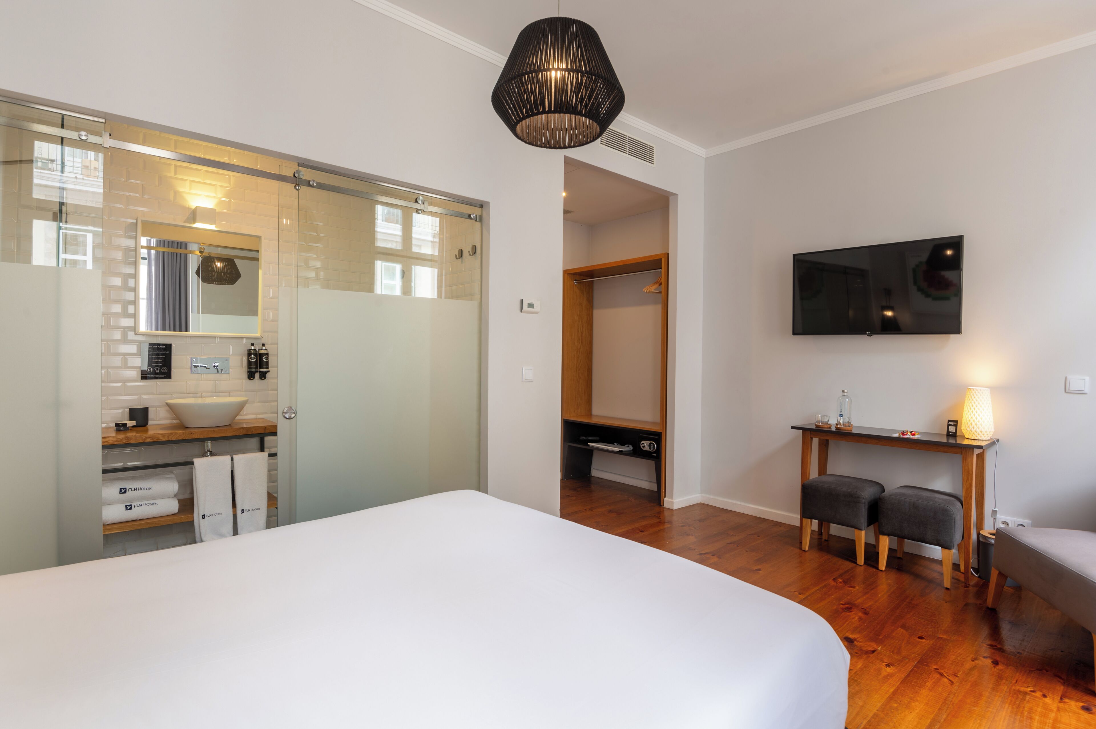 Une chambre avec un grand lit, une douche en verre, un bureau en bois avec une télévision et un placard.