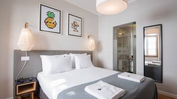 A neatly made bed with white linens, a small bedside table with a lamp, and two framed pictures on the wall.