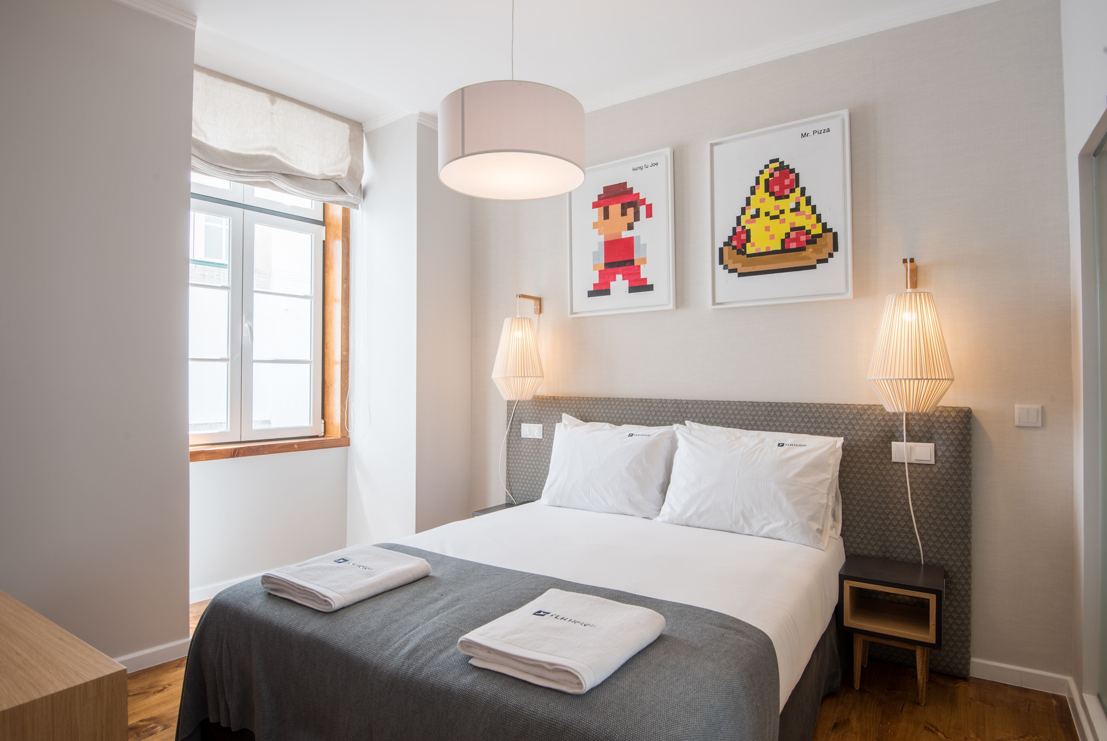 Una camera d'albergo moderna con un letto grande, due comodini, una finestra con tenda bianca e due lampade a parete.